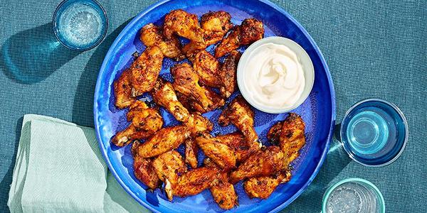 Blue plate loaded with chicken wings with a small side of garlic mayo